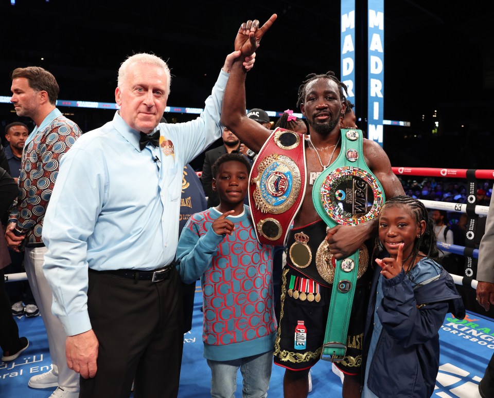 Terence Crawford with his championship belts, flanked by a referee and two children.